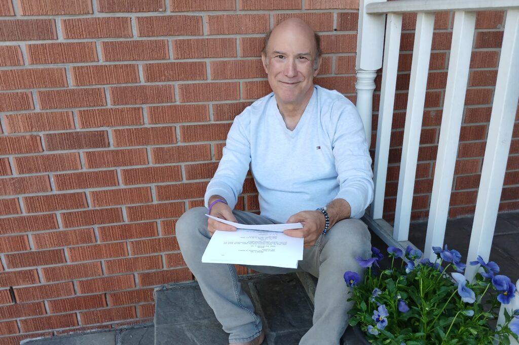 Raymond Beauchemin sits on the steps of a a home, holding a script
