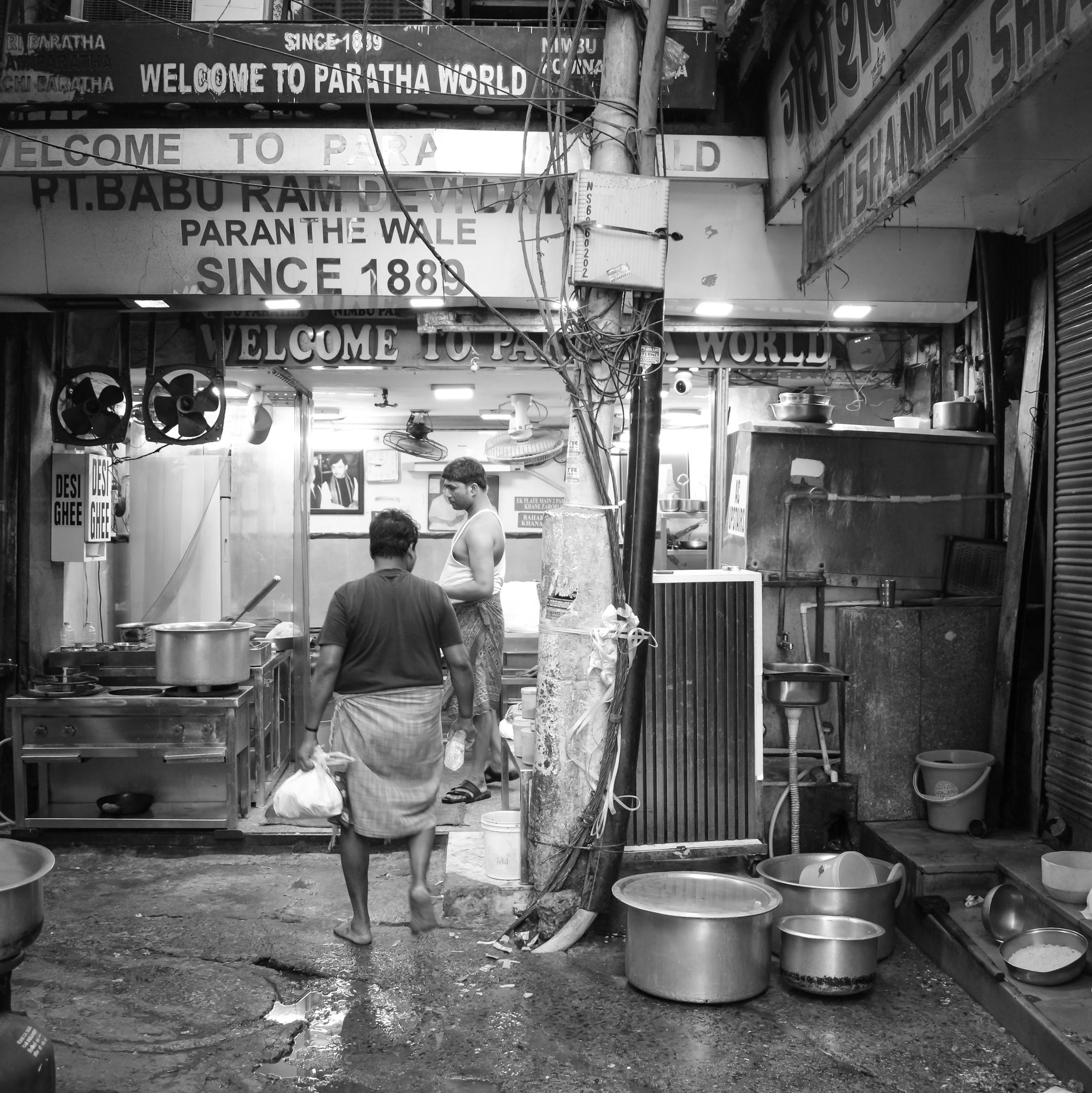 Black and white photo of people at a bustling paratha shop in Old Delhi, India.