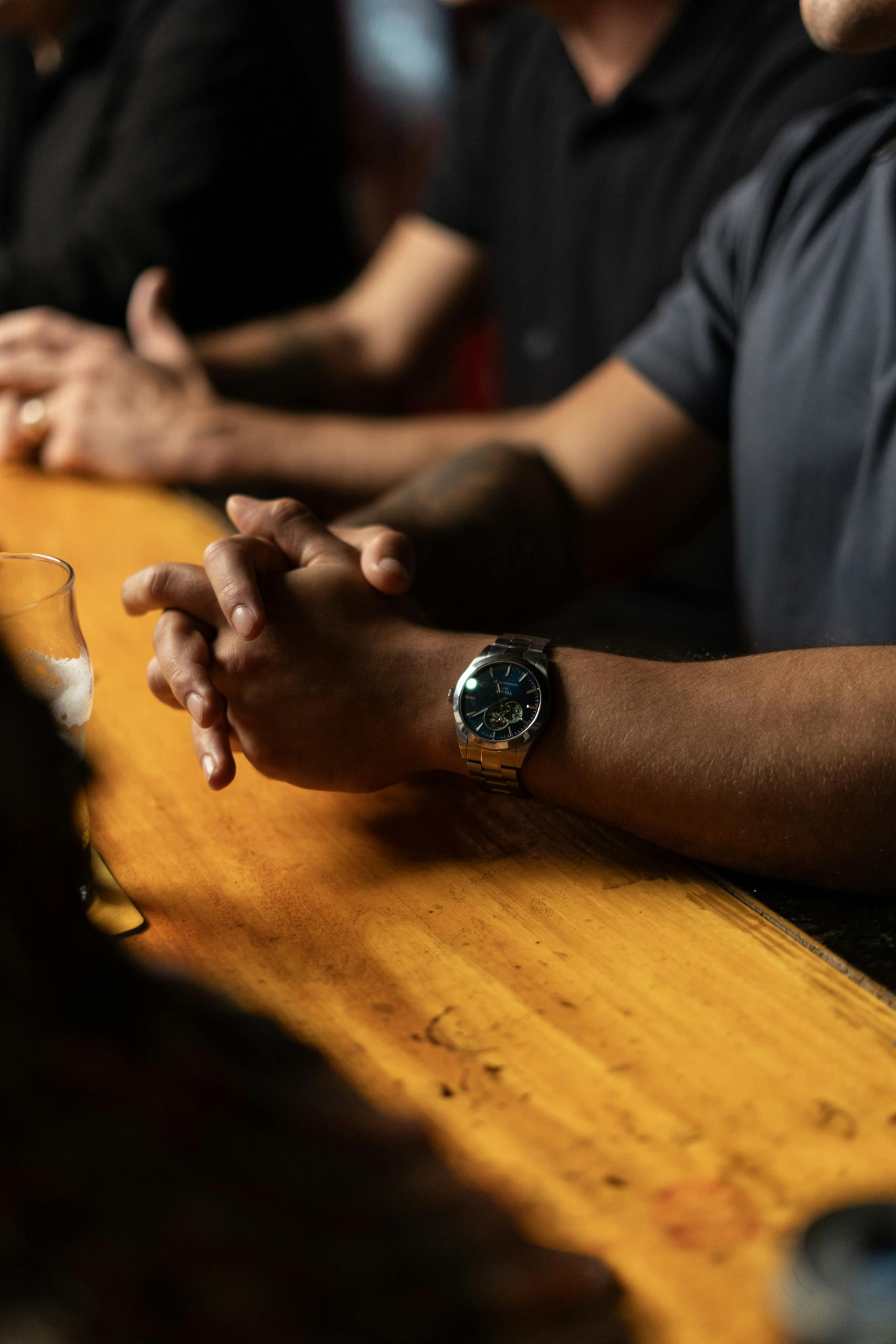 Close-up of arms resting on bar counter, highlighting a wristwatch, creating a relaxed atmosphere.